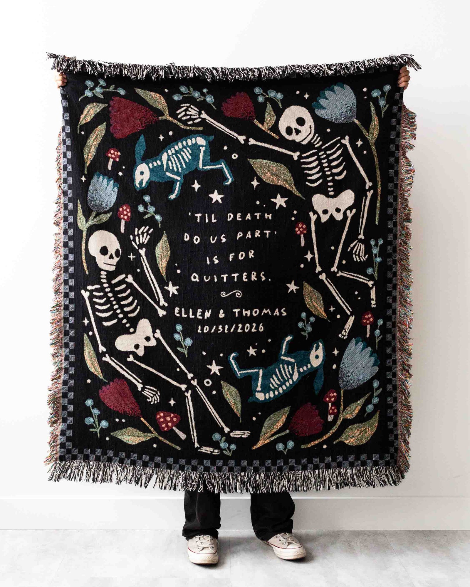 A gothic-style blanket with a black background featuring dancing skeletons, floral patterns, and the text 'Til death do us part is for quitters.' Personalization options include adding names and a date.