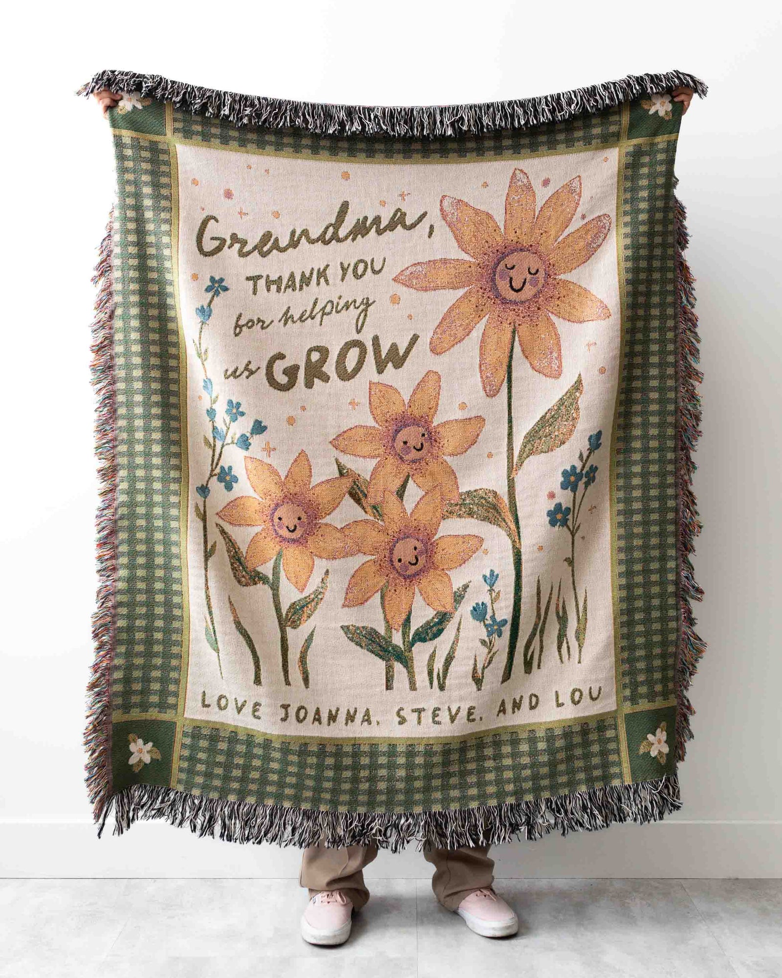 Blanket with floral design and text held by a person, against a white background
