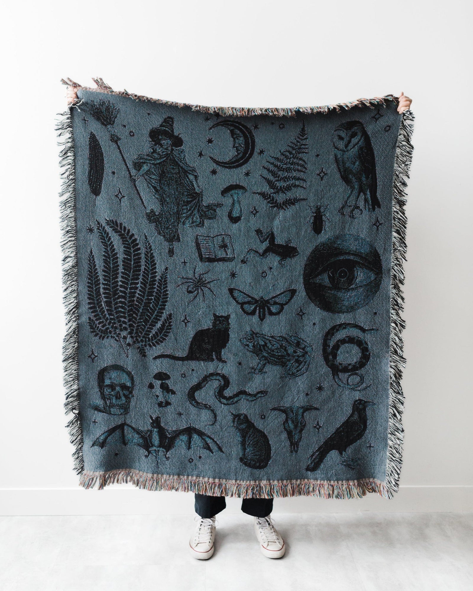Person holding a blue blanket with black illustrations of nature and fantasy elements.