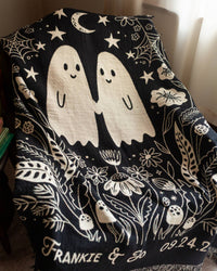 Black woven throw blanket with white ghost design and personalized names text, held by a person wearing white sneakers.