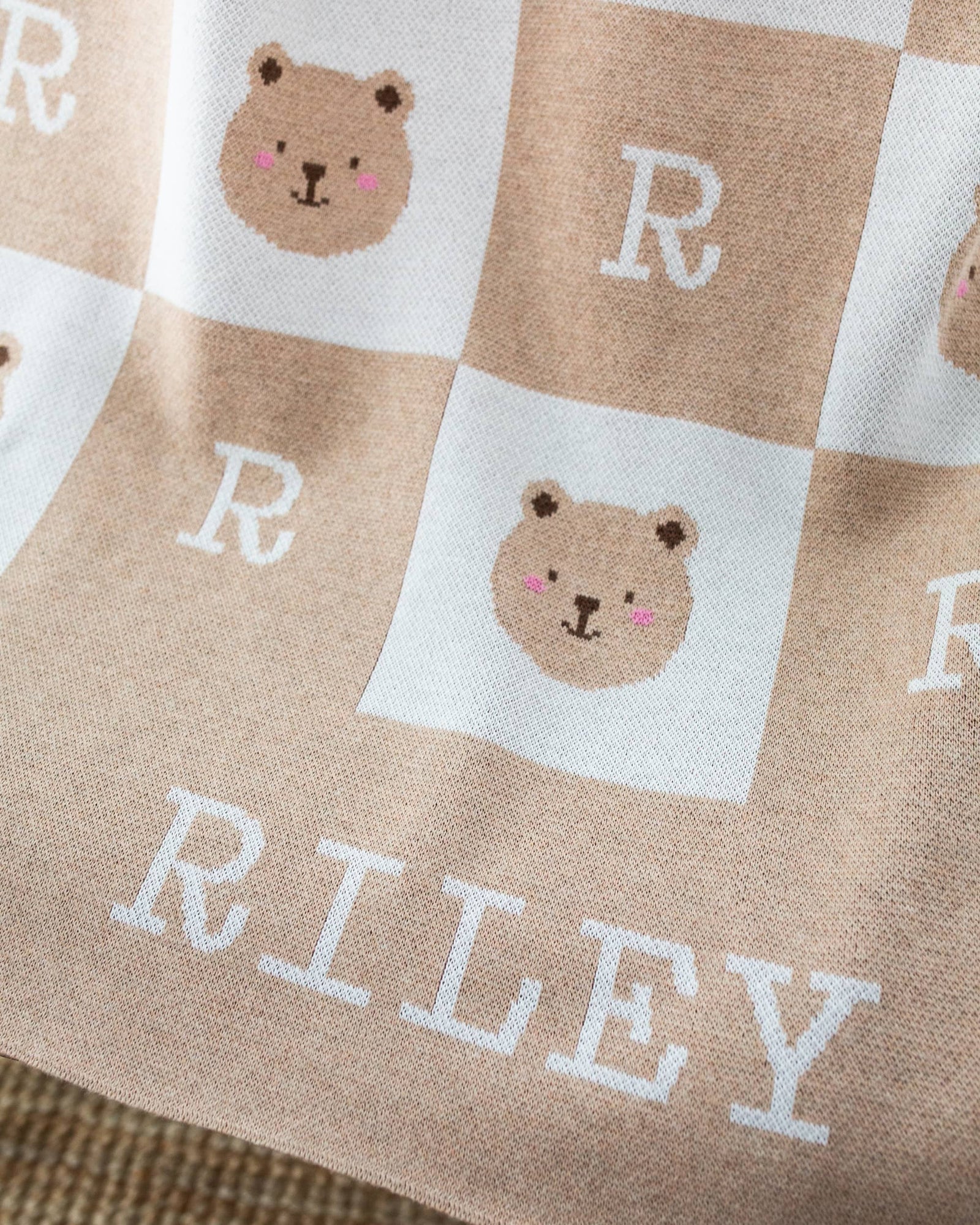 Baby blanket with teddy bear patterns and the name 'RILEY' on a chair.