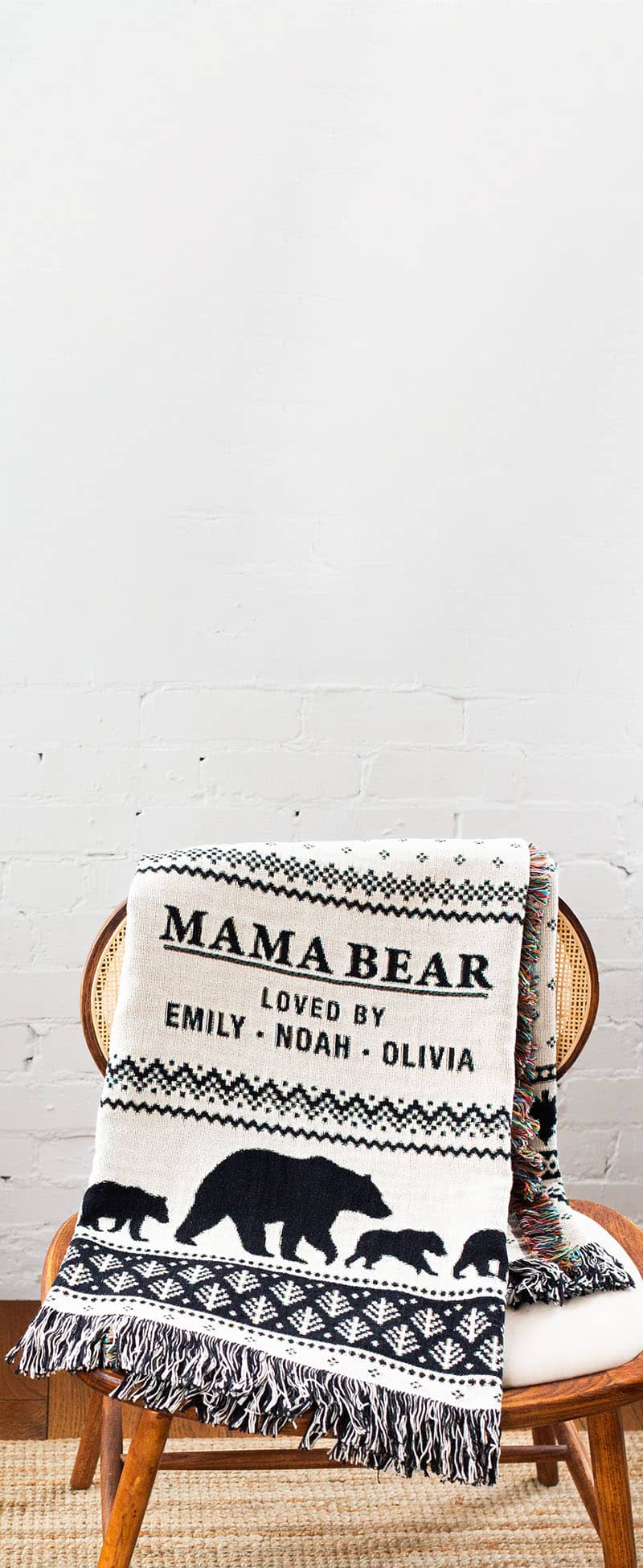 Blanket with 'Mama Bear' text and bear illustrations on a wooden chair against a white wall.