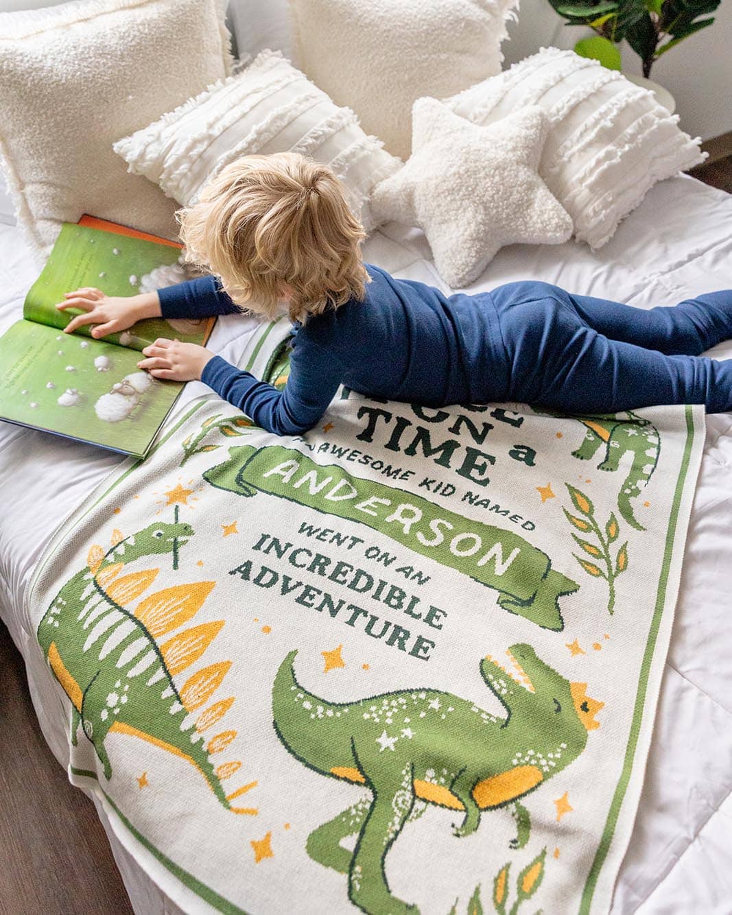 Child lying on a dinosaur-themed knit blanket with personalized text on a bed.
